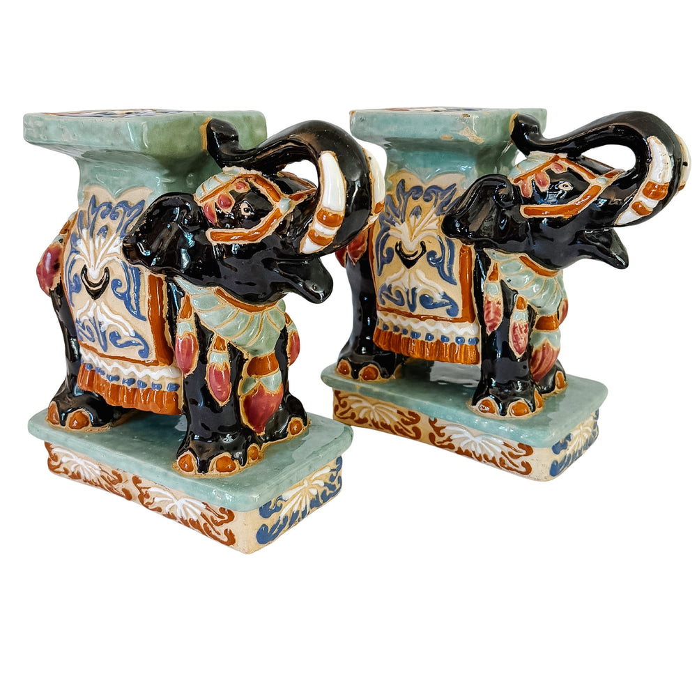 A pair of decorative ceramic elephant bookends on a white background. The bookends feature intricately painted elephants in black, orange, and cream, standing on a light blue-green base with a matching rectangular top.
